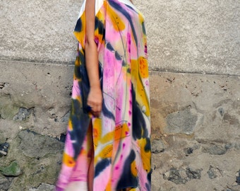 Puede incluir: Una mujer con un vestido maxi de estampado abstracto blanco y rosa, un top blanco y gafas de sol blancas. Está de pie frente a una pared de piedra.