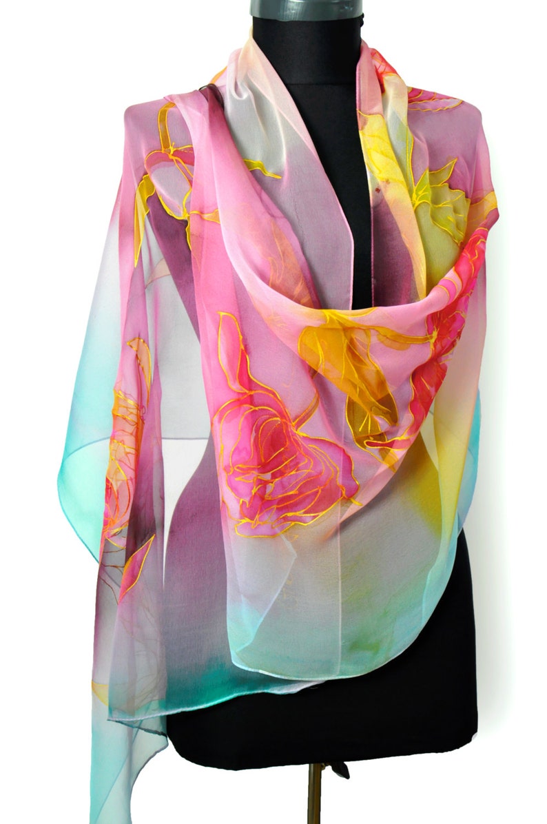May include: A pink, yellow, and turquoise silk scarf with a floral design. The scarf is draped over a black mannequin.