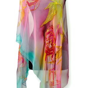 May include: A sheer silk scarf with a colorful ombre design featuring pink, yellow, and blue hues. The scarf is decorated with hand-painted floral motifs in shades of red and gold.
