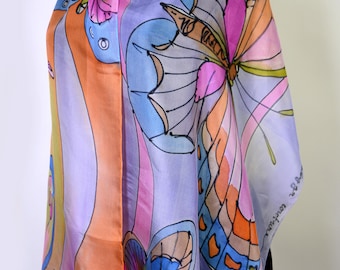 Puede incluir: Bufanda de seda colorida con diseño de mariposas. La bufanda presenta una vibrante paleta de colores rosa, naranja, azul y morado. El patrón de mariposas está delineado en negro, agregando contraste. La bufanda está drapeada sobre una forma negra.