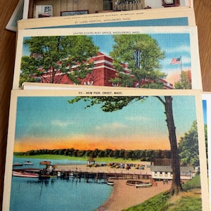 May include: A stack of vintage rectangular postcards featuring various Massachusetts landmarks. The top postcard depicts a pier at sunset in Onset, Mass., while others show the United States Post Office in Middleboro and St. Lukes Hospital.