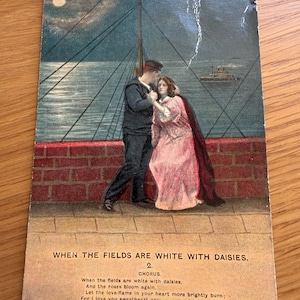 Könnte beinhalten: Eine alte Postkarte mit einem Seemann in dunkler Uniform und einer Person in einem langen rosa Kleid an einer Backsteinmauer am Meer bei Nacht. Der Text lautet: WHEN THE FIELDS ARE WHITE WITH DAISIES. 2. CHORUS. When the fields are white with daisies.