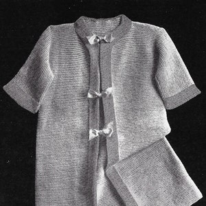 May include: A short-sleeved, knee-length knitted cardigan in a light shade, featuring a ribbed texture throughout. The garment has a round neckline, a vertical front placket with three small decorative bows, and wide cuffs on the sleeves.