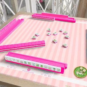 Può includere: Un set da Mahjong con un tappetino da gioco a righe rosa chiaro con istruzioni stampate, quattro supporti per tessere rosa acceso, tessere bianche con grafiche verdi e nere e un piccolo piatto rotondo verde con due dadi bianchi e una tigre.