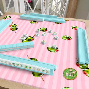 Peut inclure: Un jeu de mah-jong comprenant des réglettes bleu clair et des tuiles blanches ornées de symboles verts et colorés. Le jeu est disposé sur un tapis à rayures roses et blanches décoré d'olives vertes et de deux petits dés.