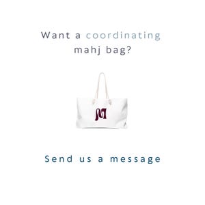 May include: A white tote bag with two white rope handles and a dark maroon letter M logo on the front. The text above the bag reads "Want a coordinating mahj bag?" and the text below the bag reads "Send us a message" in dark blue lettering.