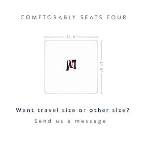 May include: A square white table with a dark maroon letter M in the center. The table measures 31.5 inches by 31.5 inches. Text above reads COMFTORABLY SEATS FOUR. Text below reads Want travel size or other size? Send us a message.