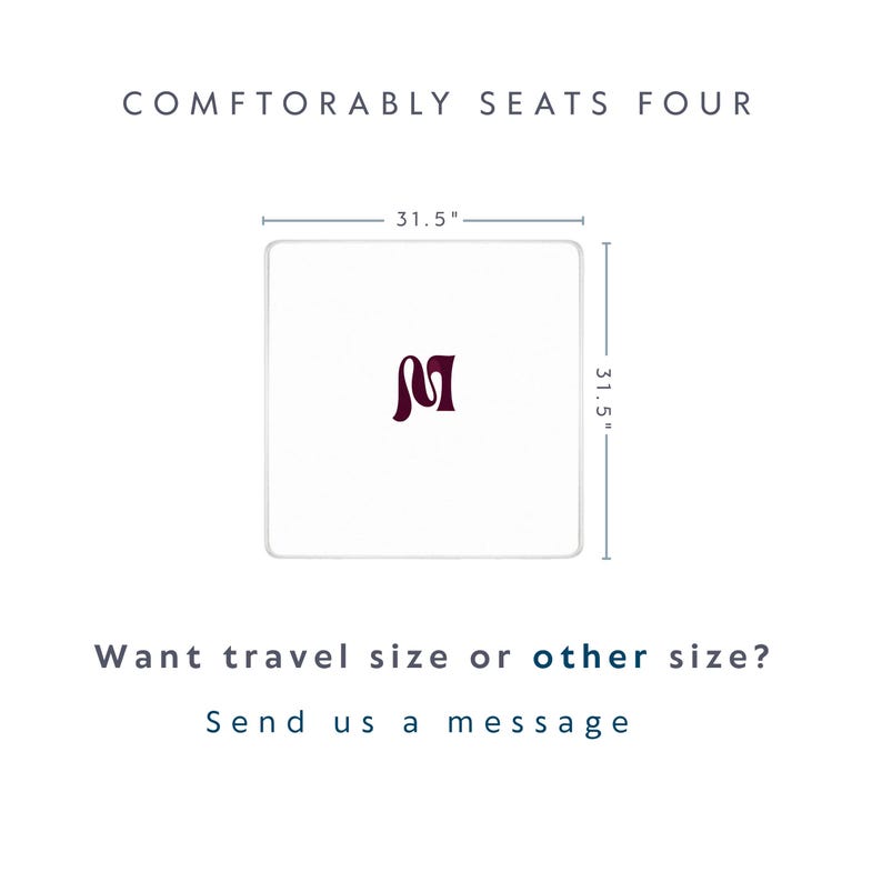 May include: A square white table with a dark maroon letter M in the center. The table measures 31.5 inches by 31.5 inches. Text above reads COMFTORABLY SEATS FOUR. Text below reads Want travel size or other size? Send us a message.