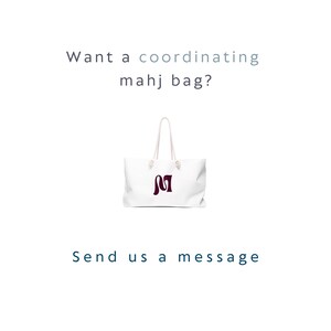 May include: A white tote bag with two white rope handles and a dark maroon letter M logo on the front. The text above the bag reads "Want a coordinating mahj bag?" and the text below the bag reads "Send us a message" in dark blue lettering.