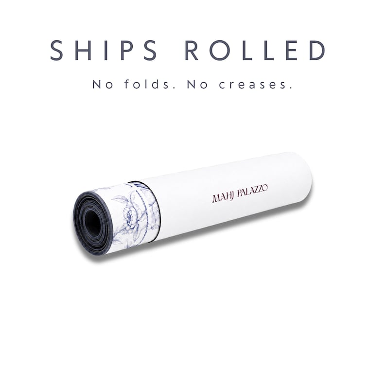 May include: A rolled mat featuring a white exterior with the text MAHJ PALAZZO in dark lettering. The inner layer displays a blue and white floral pattern. Above the mat, the text reads SHIPS ROLLED No folds. No creases.