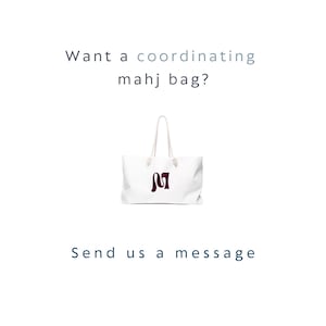 May include: A white tote bag with two white rope handles and a dark maroon letter M logo on the front. The text above the bag reads "Want a coordinating mahj bag?" and the text below the bag reads "Send us a message" in dark blue lettering.