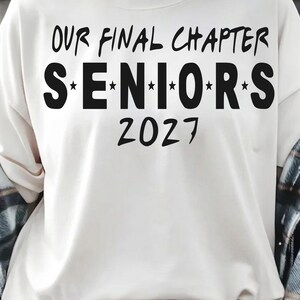 May include: A cream-colored sweatshirt featuring black text that reads "OUR FINAL CHAPTER" at the top, followed by "S*E*N*I*O*R*S" with stars between each letter, and the year "2027" printed in a bold, stylized font on the front of the garment.