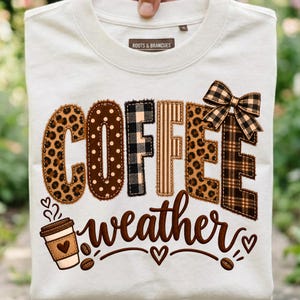 Peut inclure: Un t-shirt couleur crème avec le mot COFFEE en grandes lettres avec des motifs léopard, à carreaux et bruns. Un nœud à carreaux orne la lettre E. En dessous, le mot weather est écrit en lettres cursives brunes avec une tasse et des grains.