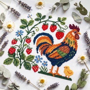 May include: A cross-stitch embroidery on white fabric featuring a colourful rooster with orange, yellow, and blue feathers standing next to a small yellow chick. The design includes green strawberry vines with red berries and small blue flowers.