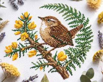May include: A cross-stitch embroidery on white fabric featuring a brown bird perched on a branch with yellow flowers and green fern-like foliage. The design is surrounded by dried lavender, yellow strawflowers, and green eucalyptus leaves.