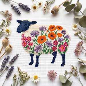 May include: A cross-stitch embroidery on white fabric featuring a sheep with a dark blue head and legs. The body of the sheep is filled with a colourful floral pattern consisting of orange poppies, purple cornflowers, and pink blossoms.