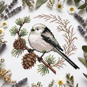 May include: A cross-stitch embroidery pattern on white fabric featuring a small bird with white, grey, and black plumage perched on a brown pine branch with two brown pinecones and green needles, surrounded by a delicate brown leafy wreath.