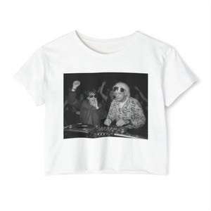 May include: A white short-sleeved t-shirt featuring a black and white graphic print on the chest. The print depicts two individuals behind a DJ mixing console, with one person wearing sunglasses and raising a fist, and the other wearing goggles.