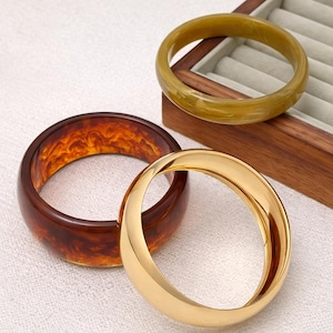 Peut inclure: Trois bracelets de différentes couleurs. L'un est de couleur or massif, un autre est de couleur ambre translucide et le troisième est de couleur vert olive translucide. Les bracelets sont ronds et semblent être en résine ou en métal.