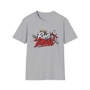 May include: A heather gray short-sleeve t-shirt featuring a graphic print with the text Run Devil in white and red script. The design includes a gold crown, a white cross with a red cloth draped over it, and black chains on a gray background.