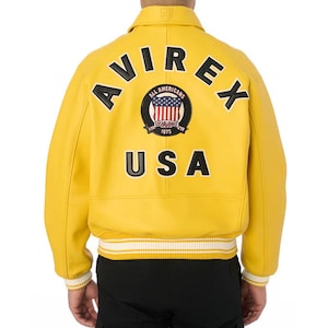 Pu&ograve; includere: Giacca in pelle giallo brillante con la scritta "AVIREX" ad arco sulle spalle. Sotto, una toppa circolare con le parole "ALL AMERICANS" e "ESTABLISHED 1975" che circondano un disegno della bandiera americana. La parola "USA" &egrave; stampata sotto.