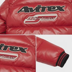Pode incluir: Casaco acolchoado vermelho com o nome da marca "Avirex" em letras pretas e brancas. O casaco tamb&eacute;m apresenta o texto "All Star Dualers" num emblema vermelho e branco. O punho da manga tem riscas pretas e vermelhas.