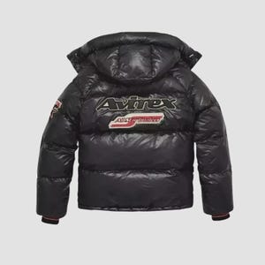 Pode incluir: Casaco puffer preto com capuz. O casaco apresenta o logotipo "Avirex" nas costas, juntamente com "All Star Lumberjacks". O casaco tem um acabamento brilhante e um punho listrado vermelho e preto.