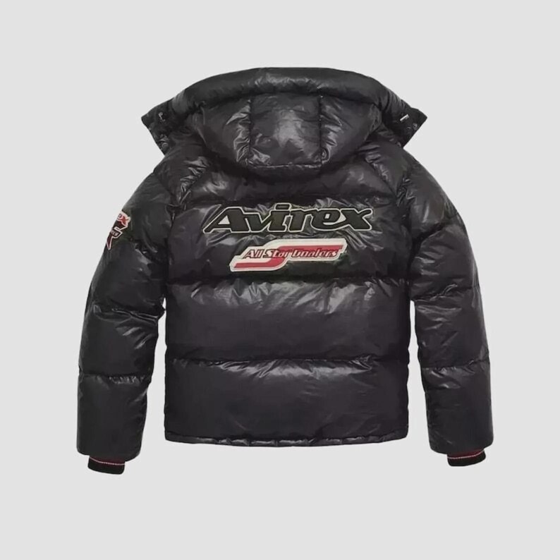 Pode incluir: Casaco puffer preto com capuz. O casaco apresenta o logotipo "Avirex" nas costas, juntamente com "All Star Lumberjacks". O casaco tem um acabamento brilhante e um punho listrado vermelho e preto.