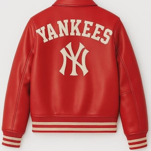 Può includere: Giacca rossa dei Yankees con scritte e logo bianchi. La giacca presenta un classico stile baseball con colletto, polsini e orlo a coste. Il logo degli Yankees è ben visibile sul davanti.