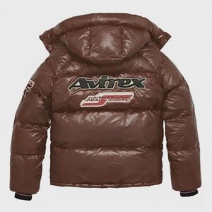 Pode incluir: Casaco puffer castanho com capuz. O casaco apresenta o nome da marca "Avirex" em letras brancas e pretas nas costas, com "All Star Dealers" por baixo. O casaco tem um acabamento brilhante e um design acolchoado.