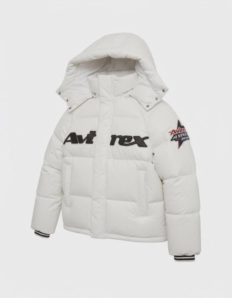 Pode incluir: Um casaco acolchoado branco com capuz. O casaco apresenta o texto "Avi rex" em preto no peito e um patch na manga. Os punhos t&ecirc;m riscas brancas e pretas.
