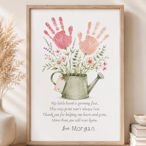May include: A framed wall art print featuring a green watering can with a bouquet of flowers made from two handprints in shades of pink and peach. Below the illustration is the text: My little hand is growing fast, This tiny print won't always last. Thank you for helping me learn and grow, More than you will ever know. Love, Morgan.