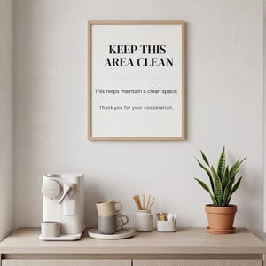 以下が含まれることがあります： 「KEEP THIS AREA CLEAN」の文字が入った額縁入りの看板がカウンターの上に飾られています。コーヒーメーカー、マグカップ、鉢植えのサンスベリアがカウンターに置かれています。看板には「This helps maintain a clean space」と「Thank you for your cooperation」というフレーズも含まれています。