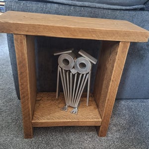 May include: A rectangular wooden side table with a natural brown grain finish and a lower shelf. Positioned on the lower shelf is a metallic owl sculpture constructed from silver-coloured metal components, including circular eyes and flat metal plates.