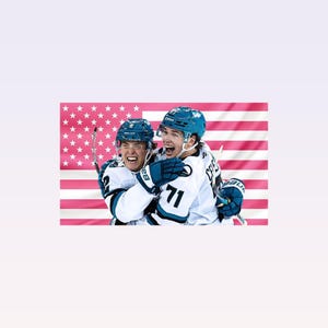 Könnte beinhalten: Zwei Eishockeyspieler in weißen und tealfarbenen Trikots umarmen sich jubelnd. Sie tragen Helme und Handschuhe, wobei die Nummer 71 auf einem Trikot zu sehen ist. Im Hintergrund ist eine pinkfarbene amerikanische Flagge.