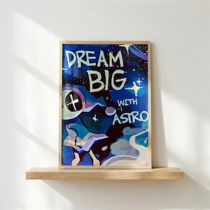 Könnte beinhalten: Gerahmter Kunstdruck mit den Worten "DREAM BIG" und "WITH ASTRO" in Weiß und Hellgrün. Das Kunstwerk zeigt eine blau-violette Weltraum-Illustration mit einer Figur und Sternen.