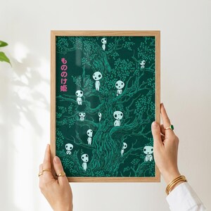 May include: A framed art print featuring a dark green illustration of a tree with numerous white, spirit-like figures. The Japanese text "もののけ姫" is printed in pink on the left side. The print is held by hands with gold rings and bracelets.