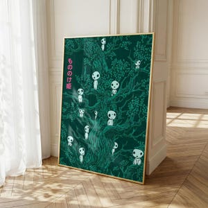 May include: A framed art print featuring a dark green illustration of a tree with white spirit figures. The artwork has a gold frame and the Japanese text "もののけ姫" in pink on the left side. The print is leaning against a wall.