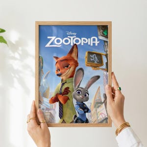 Pode incluir: Um poster emoldurado do filme da Disney "Zootopia". O poster apresenta os personagens Nick Wilde, uma raposa, e Judy Hopps, uma coelha, contra um cen&aacute;rio urbano. O poster &eacute; segurado por uma pessoa.