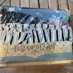 May include: A full sheet set by Elizabeth Gray in plastic packaging. The set includes a black fabric with a floral pattern featuring pink and blue flowers, and a white fabric with black vertical stripes. The label reads Elizabeth Gray.