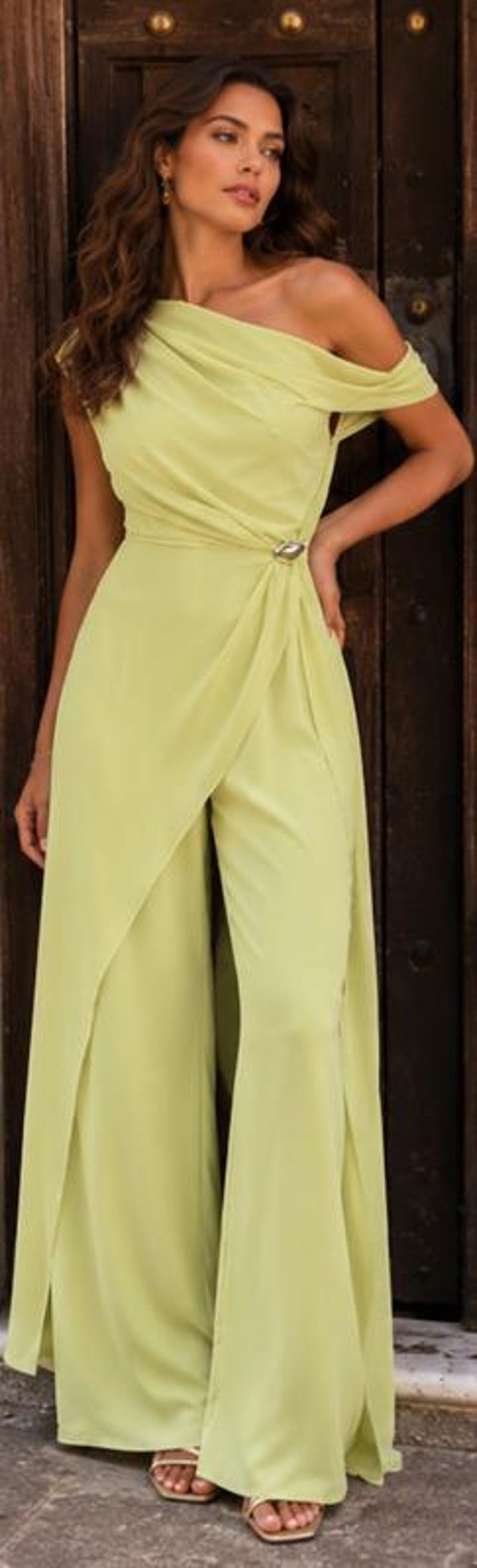 May include: A lime green jumpsuit featuring an off-the-shoulder neckline with draped fabric across the bodice. The garment includes a side waist accent with a metallic detail and wide-leg trousers with an integrated wrap-style skirt overlay.