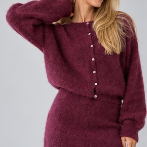 Peut inclure: Un ensemble deux pièces en maille duveteuse bordeaux foncé composé d'un cardigan à manches longues avec une encolure ronde et une rangée de petits boutons blancs sur le devant, assorti d'une mini-jupe taille haute en maille texturée.