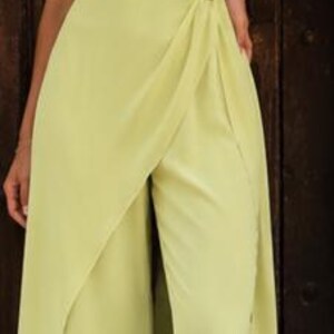 May include: A light lime green jumpsuit featuring an asymmetrical off-the-shoulder neckline with draped fabric across the bodice. The waist is accented with a silver-toned metallic detail, and the wide-leg trousers include a front overlay panel.