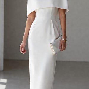 Könnte beinhalten: Weißes Midikleid mit capeartigem Überwurf. Das Kleid hat eine figurbetonte Silhouette und wird mit weißen Absätzen und einer Clutch kombiniert. Der Stil ist elegant und für formelle Anlässe geeignet. Das Kleid ist etwa 100 cm lang.
