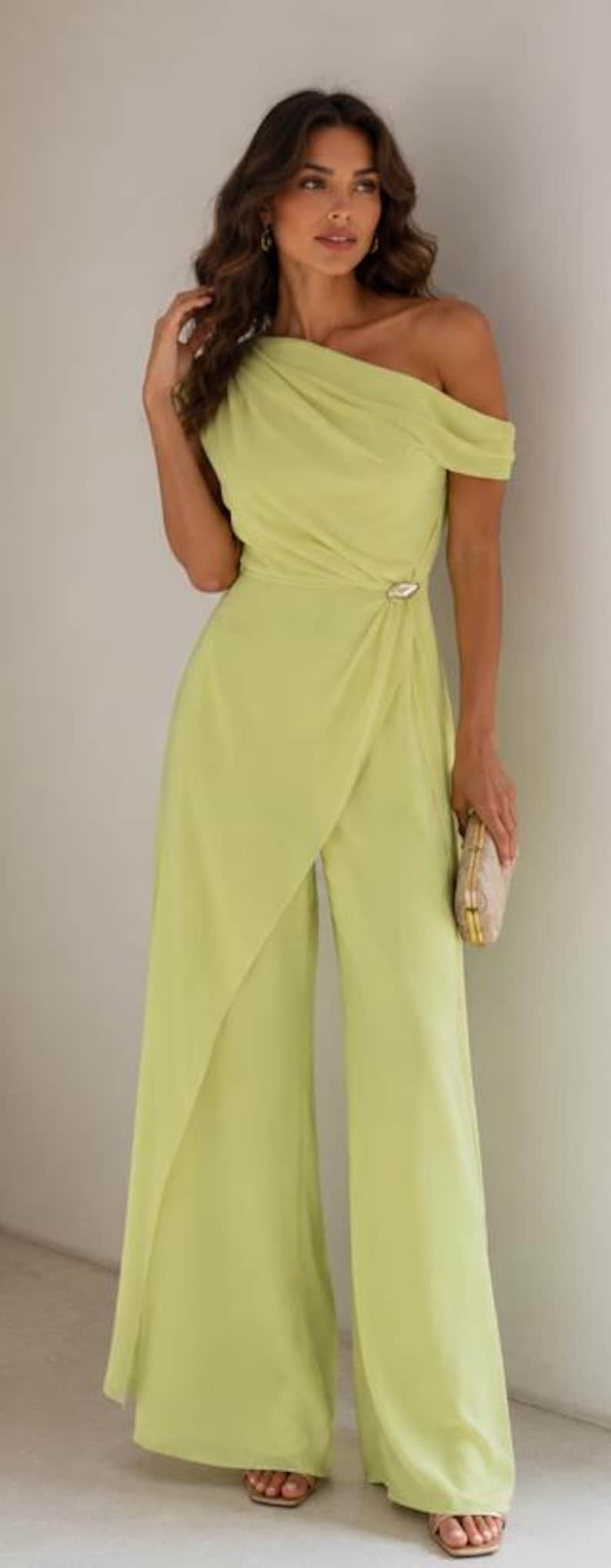 May include: A lime green one-shoulder jumpsuit featuring a draped bodice, a side waist accent with a metallic detail, and wide-leg trousers with an overlapping front panel design. The garment is floor-length and has a smooth, solid-colored fabric.