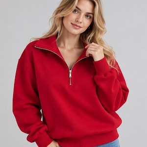 Puede incluir: Una sudadera roja de manga larga con cuello de cremallera de un cuarto, cierre de metal plateado, puños acanalados en las muñecas y dobladillo acanalado. La prenda está confeccionada con una tela de color sólido.