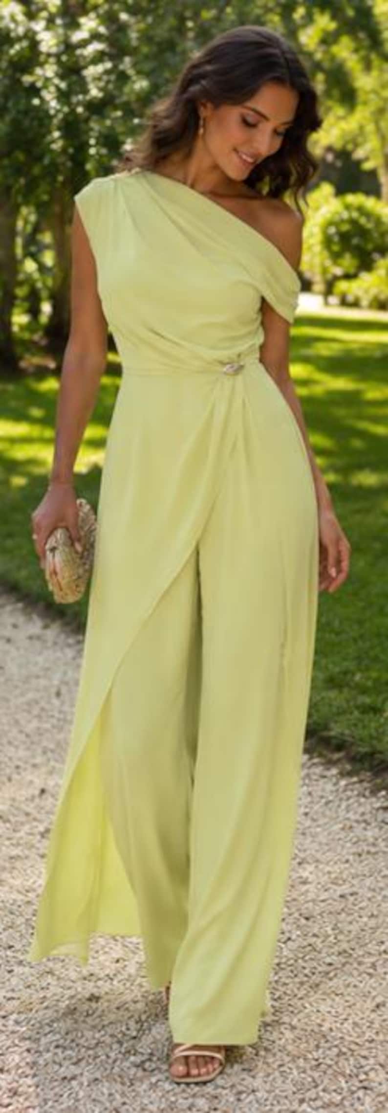 May include: A light lime green one-shoulder jumpsuit featuring a draped bodice, a gathered waist detail with a metallic accent, and wide-leg trousers with an overlay panel that creates a skirt-like appearance. The fabric has a smooth texture.
