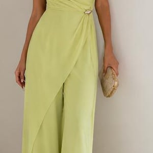 May include: A lime green one-shoulder jumpsuit featuring a draped bodice, a fitted waist with a decorative metallic accent, and wide-leg trousers with an overlapping front panel design. The garment is paired with a small gold clutch and sandals.