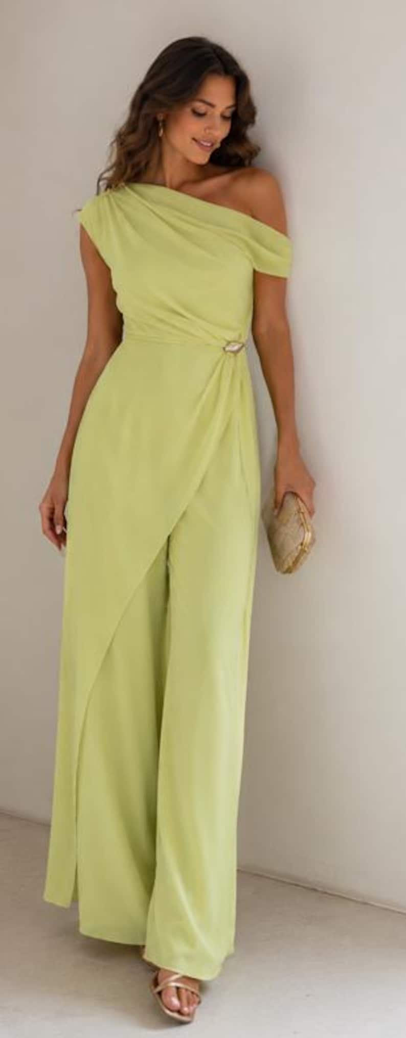May include: A lime green one-shoulder jumpsuit featuring a draped bodice, a fitted waist with a decorative metallic accent, and wide-leg trousers with an overlapping front panel design. The garment is paired with a small gold clutch and sandals.