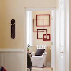 May include: A vertical, oval-shaped wall clock made of dark brown wood with a visible grain pattern. The clock features bright yellow hour, minute, and second hands centered on the wood surface, providing a sharp contrast to the dark wood.